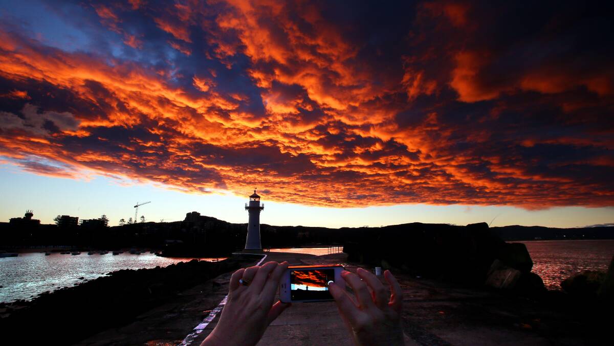 Fiery looking clouds look in the sky as the sunsets over the Illawarra on the break wall and lighthouse at Wollongong Harbour. Picture: KIRK GILMOUR