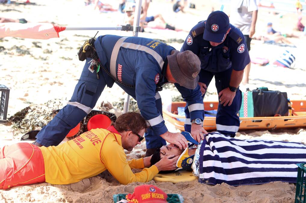 SPINAL PRECAUTIONS: A surf lifesaver and paramedics treat a man injured in the surf at North Wollongong. Picture: Sylvia Liber