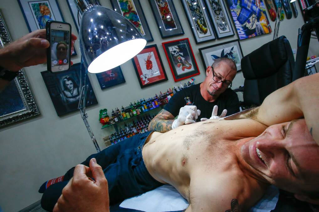 Injured surfer Brett Connellan looks on via video call as Justin Wynn gets a tattoo in his honour. Picture: Adam McLean