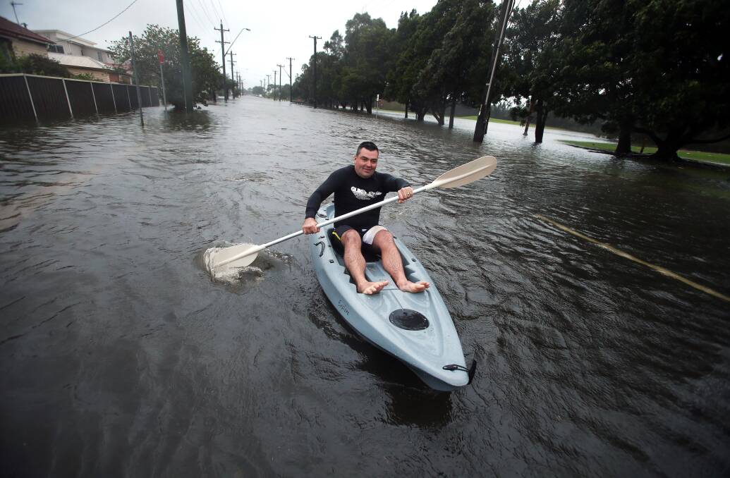 under water: Justin Craig paddles down a submerged Swan Street in Wollongong after a weekend of heavy rains hits the region. Picture: Sylvia Liber