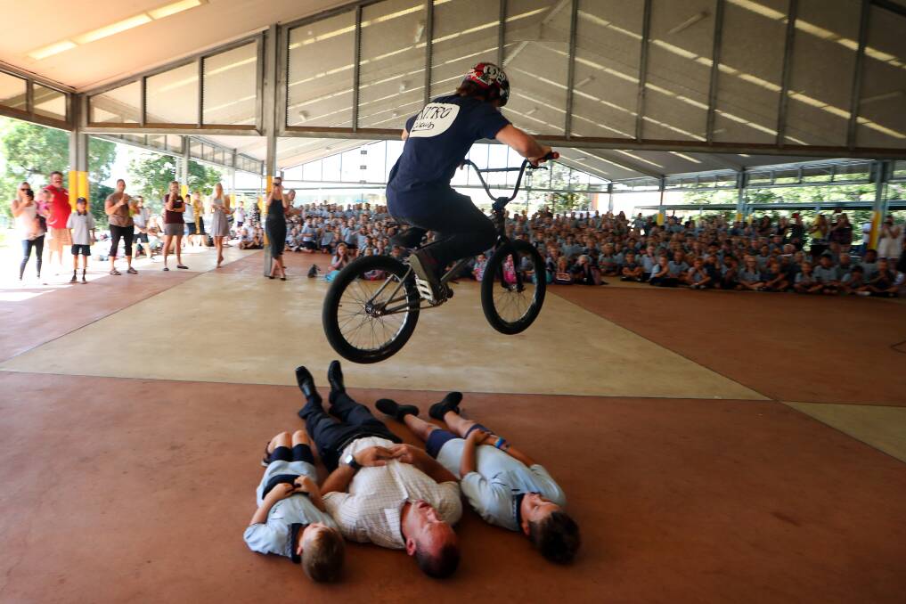 HIGH FLYING: Nitro Circus star Kurtis Downs jumps over Shell Cove Public School principal Simon Webb and students Jye Falconer and Bodhi Smith. Six of the NItro Circus crew dropped by the school on Monday. Picture: Sylvia Liber