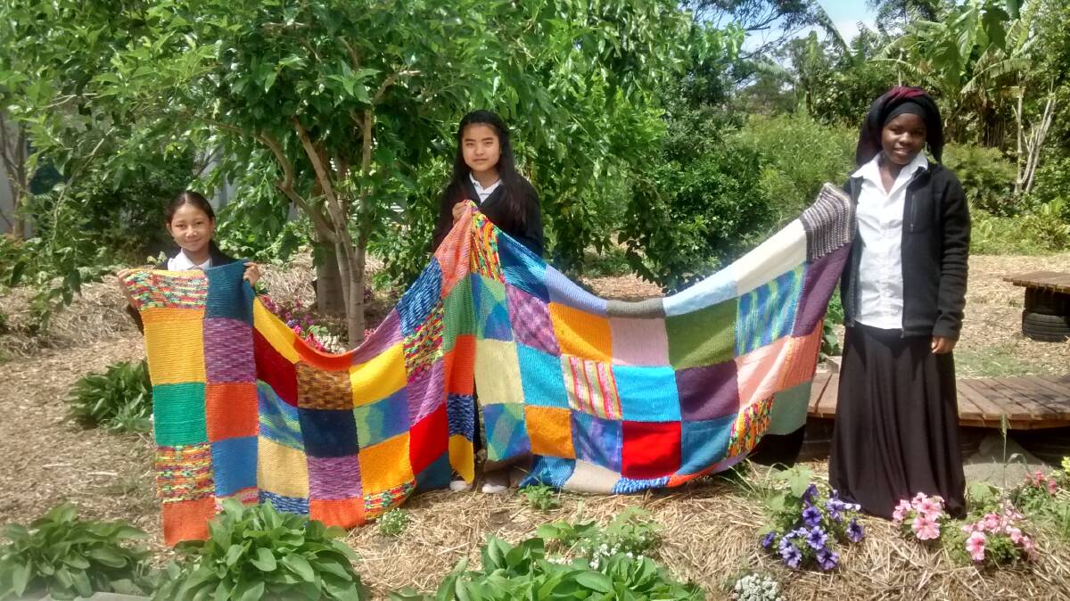 BLANKET OF LOVE: Warrawong High School IEC students Pray Meh, Lee Meh and Elena Bukuru knitted numerous squares as part of the project.