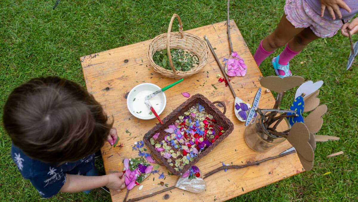 Children glue flower petals to cardboard at a craft station during play time. 