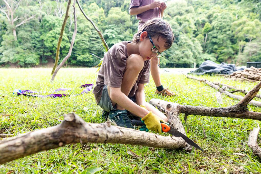 A boy saws a fallen branch during a facilitated hut-building activity. 