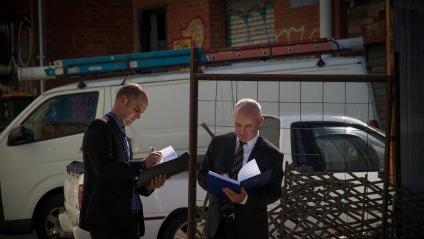 Paul Rowe (left) and Dave Butler typify the public's idea of homicide squad detectives, carrying bound folders and wearing darks suits. Photo: Supplied

