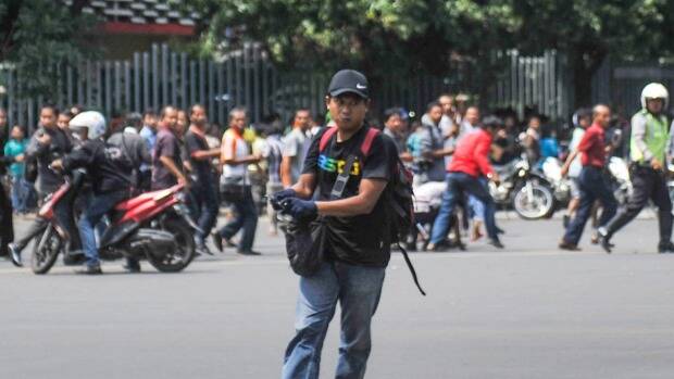 An unidentified man with a gun and a backpack walks on Thamrin Street as people run in the background near Sarinah shopping mall in Jakarta on Thursday. Photo: AP