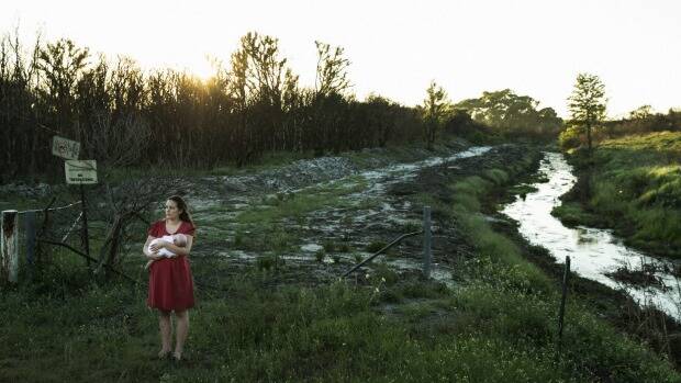 Samantha Kelly holds her baby William beside one of the drains running from the Williamtown RAAF base near Newcastle. Photo: Nic Walker