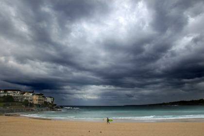 A lone surfer on Bondi Beach Christmas eve as ominous clouds signal the approaching weather system that will bring storms and another dangerous surf conditions to Sydney. Photo: Dallas Kilponen