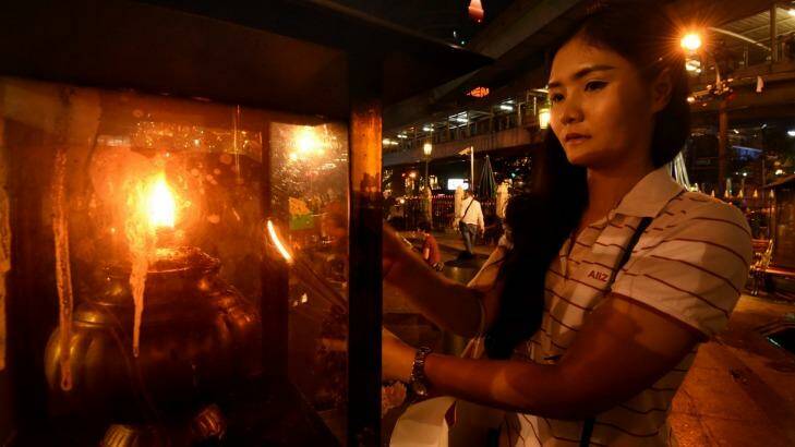 A young woman lights a candle before praying at Erawan Shrine in Bangkok on Thursday.  Photo: Kate Geraghty