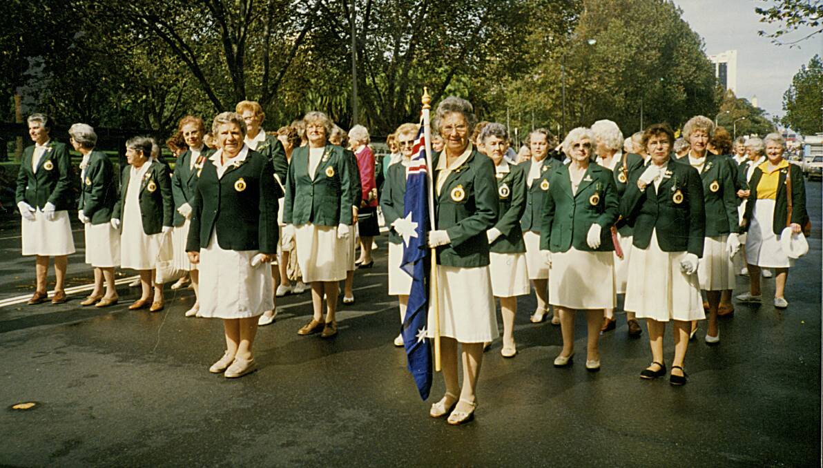 Betty Brown holding the Australian flag during an Anzac Day march with fellow former AWLA members in their green and cream uniforms.