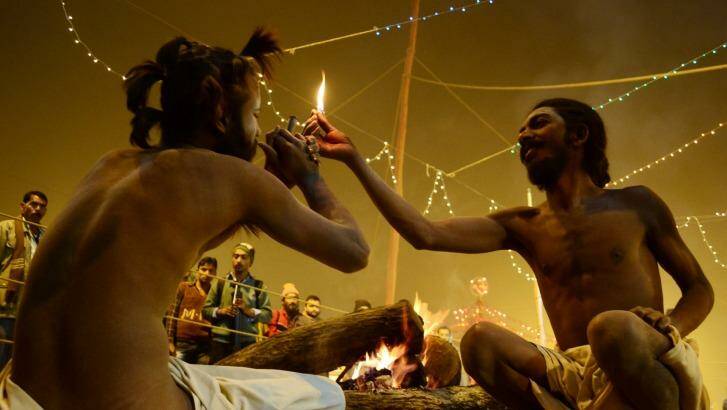  A Naga Sadhu gets ready to smoke a chillum  as another strikes the match to light it  in their camp in the Kumbh Mela area.   Photo: Hindustan Times