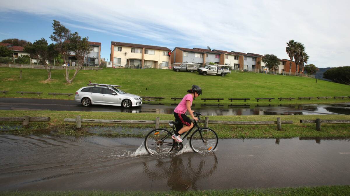 A cyclist makes her way through a flood at Bellambi after a water main burst on Thursday (above). Picture: KIRK GILMOUR