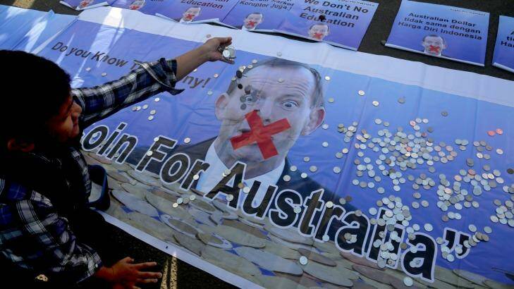 An Indonesian man throws money onto a poster of Prime Minister Tony Abbott in February, after Mr Abbott linked aid to Indonesia with the cases of Bali nine pair Andrew Chan and Myuran Sukumaran.   Photo: Tatan Syuflana