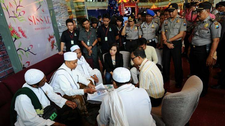 Police look on at a Surabaya shopping centre as centre staff sign a document promising not to dress employees in Christmas apparel. Photo: Robertus Pudyanto