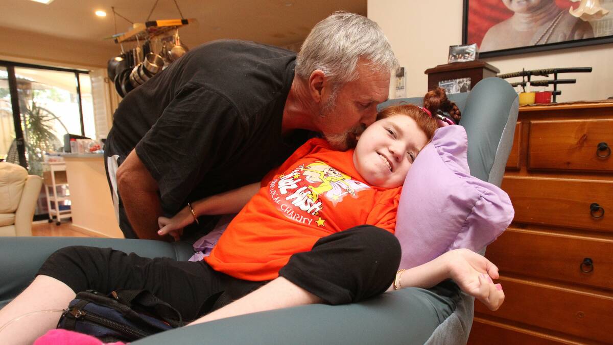 Abbie Tippin get a kiss from her grandfather, Steve Amey, as she rests in her new mobility chair. Picture: GREG TOTMAN