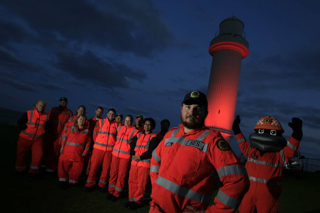 Wollongong SES volunteer David Swyer and fellow volunteers stand under an orange Wollongong Lighthouse. Picture: ANDY ZAKELI