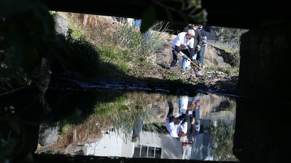 Volunteers remove rubbish from the clogged creek that runs through Corrimal. Picture: KIRK GILMOUR