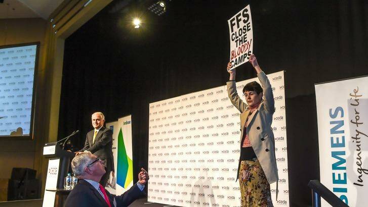 The lone protester holds up her sign while Malcolm Turnbull halts his speech. Photo: Justin McManus