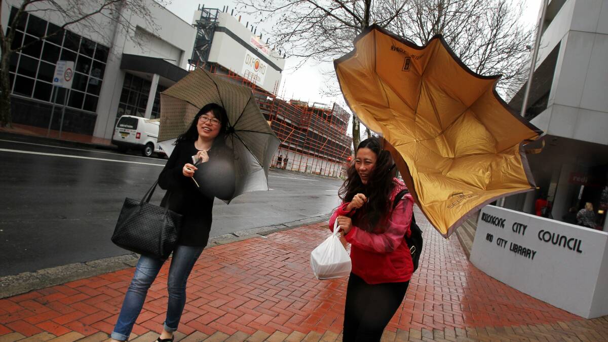 Juan Wang and Rui Yin struggle with the rain and wind in Burelli St, Wollongong, today. Picture: SYLVIA LIBER