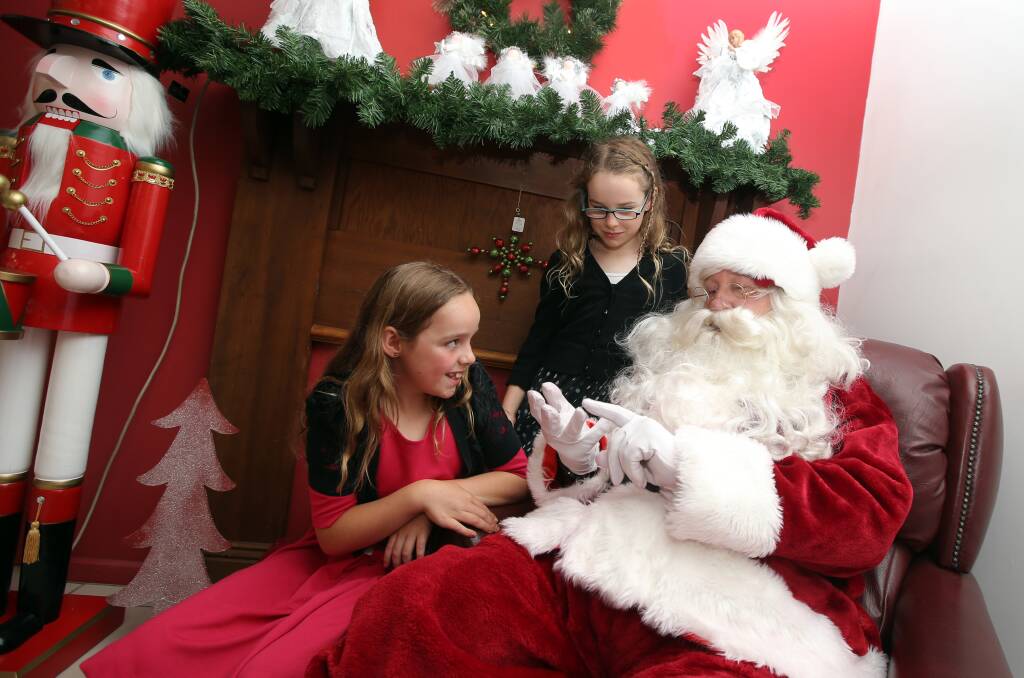 Warrnambool’s Kaitlyn Barnett, 10, and her sister Freya, 8, discuss with Santa what they would like him to leave under their tree at the Warrnambool Christmas Shop at Centro Plaza yesterday. 141222DW03 Picture: DAMIAN WHITE