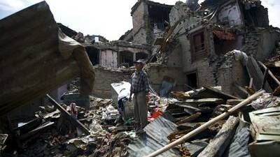 A Nepalese man stands on the debris of collapsed houses.
