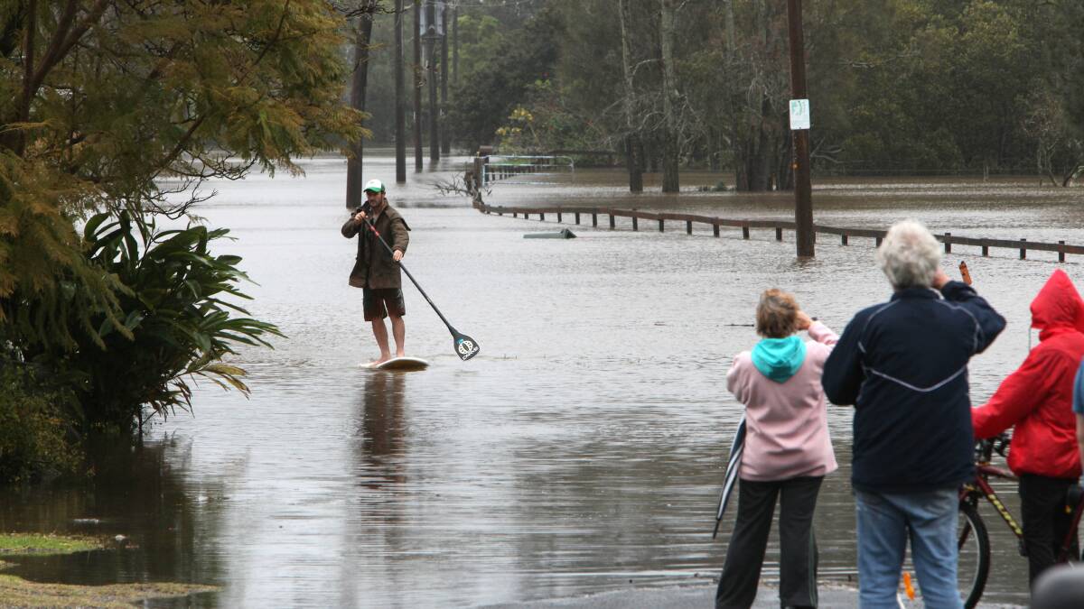 Chris White paddles his stand up surfboard on Hay Avenue at Shoalhaven Head as the Shoalhaven River continues to rise on August 26. Picture: Kirk Gilmour

