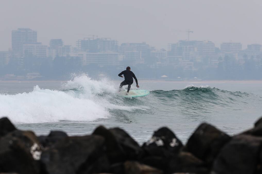 A surfer catches a wave at Towradgi beach as smoke from hazard reduction burns reduces visibility of Wollongong. Picture: Adam McLean