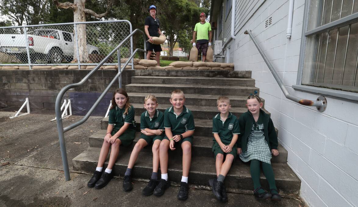 Mount Ousley Public School students Olivia Simiana, Lawson Carter, James McCrae, Luca Simiana and Emily McCrae, with (back) parents Joel Scott and Luke Smith placing sandbags to help protect the school during predicted wet weather this weekend. Picture by Robert Peet