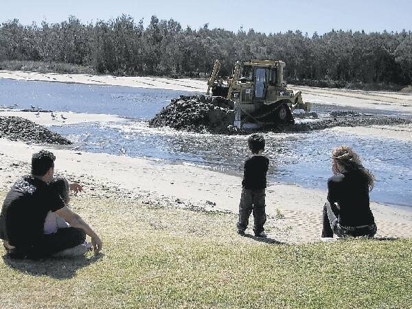 A family watches as a bulldozer works to recreate the Berageree Island channel in Lake Illawarra yesterday. The sand is being moved to Edith Lacey Park.