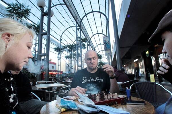 Brett Cockburn enjoys a cigarette and coffee at a cafe in Crown St Mall while playing chess. Council is considering banning smoking in the mall. Picture: ADAM McLEAN