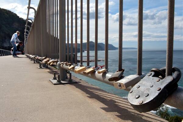 Tourists  check  out the many padlocks attached to the railings on the southern side of the Sea Cliff Bridge at Clifton. The locks –    symbols of  the permanency of relationships –  are  corroding   the bridge. Picture:  KIRK GILMOUR