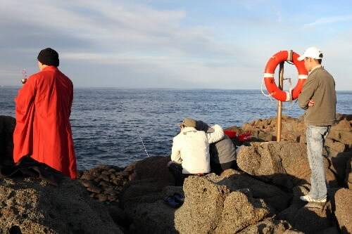 A Buddhist monk prays for a fisherman feared drowned after he was washed off rocks at Port Kembla, while relatives look on. Picture: SYLVIA LIBER