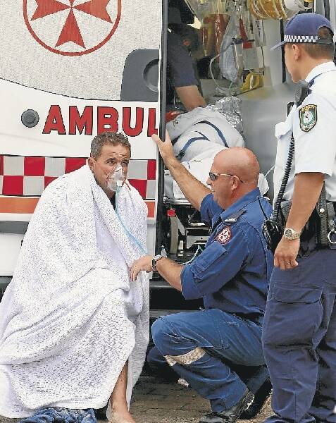 Paramedics and police officers treat one of the fishermen at Port Kembla. Pictures: KEN ROBERTSON