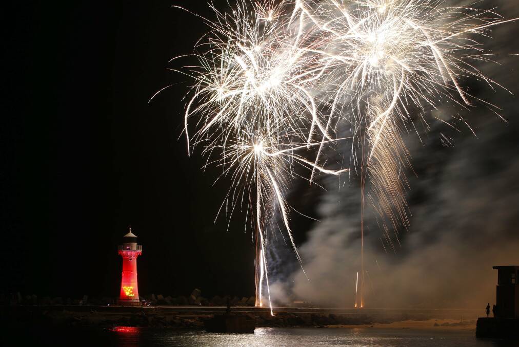 The smaller of Wollongong's two lighthouses is illuminated by pink light as fireworks erupt over Belmore Basin.