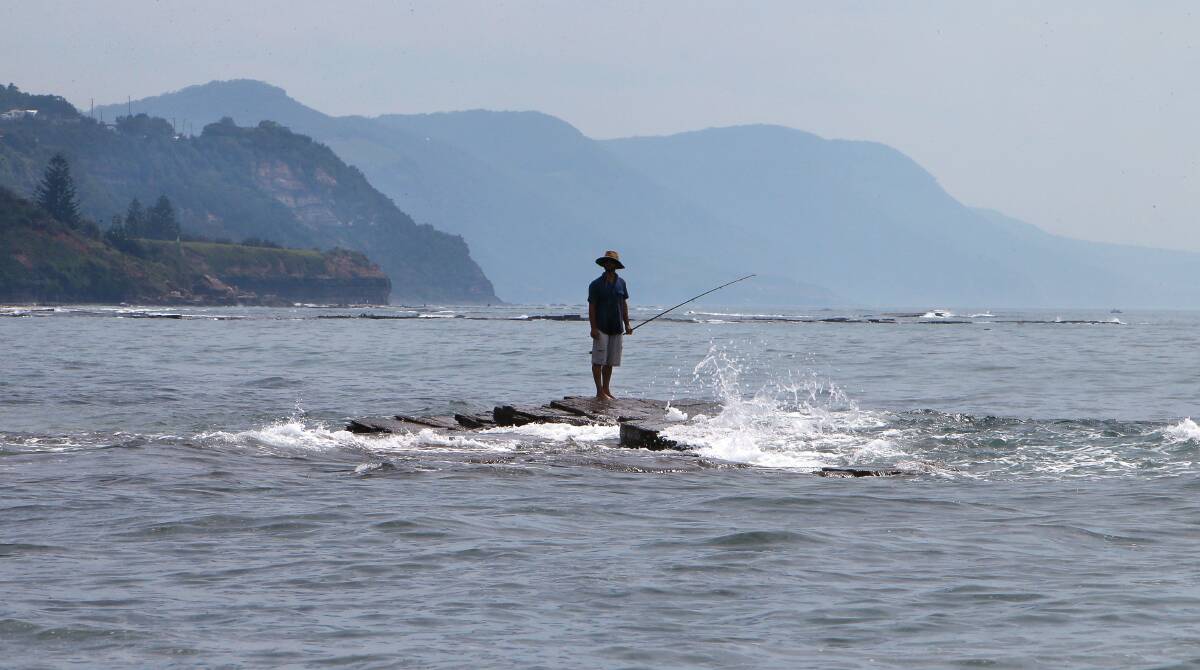 A fisherman stands on a rocky perch near the Austinmer boat ramp. Picture: KIRK GILMOUR