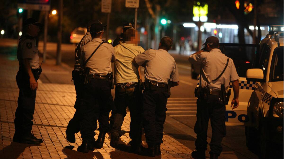 Police detain a man during a late-night operation in Wollongong. 