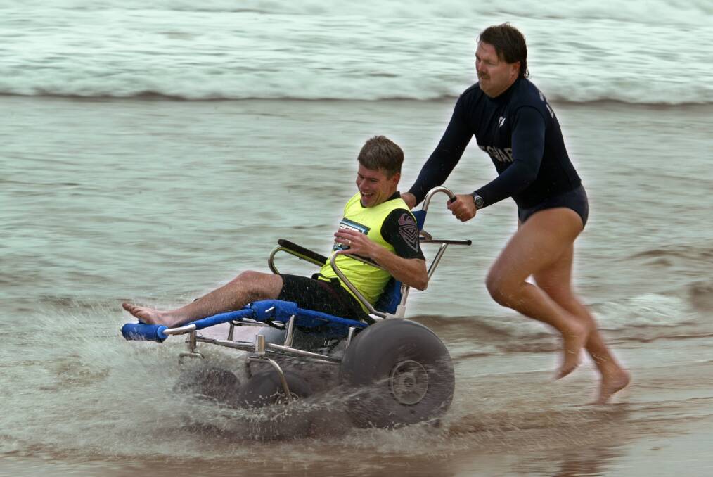 Disabled surfer Len Snowdon gets a ride in the new Free Wheelers Wheelchair from lifeguard Ian Picton at Thirroul Beach.