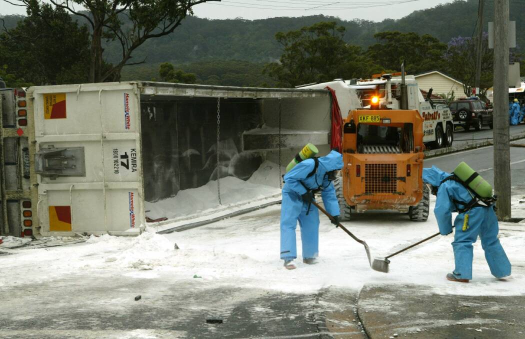 Fire officers wearing protective suits and breathing apparatus work to clear soda ash from Bulli Pass after a truck overturned.