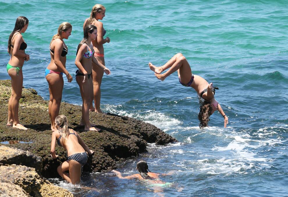 Girls cool off by jumping into the surf off rocks at Wollongong City Beach. Picture: KIRK GILMOUR