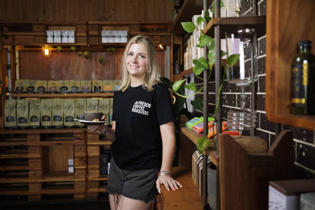 Jess Cottington, supervisor at Alfresco Coffee Roasters in Moruya, holds a cup of capppchino. Behind her are packages of Alfresco's seven single origins and six blends. Picture by Keegan Carroll