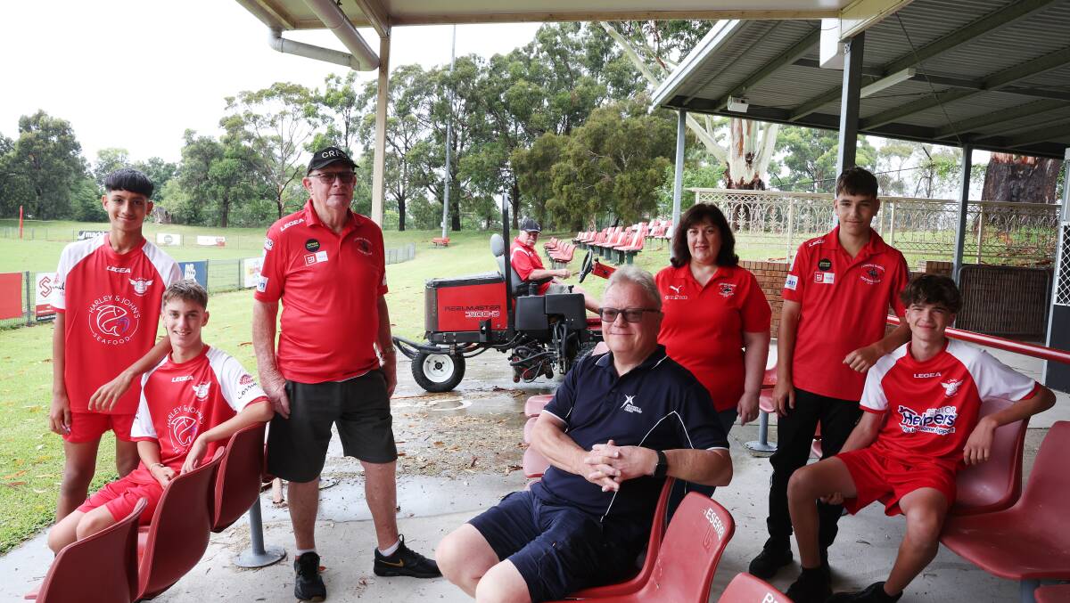 Corrimal Rangers were gifted new seats and a brand new lawn mower from WIN Stadium management after vandals destroyed parts of Memorial Park earlier this year. Pictured is Arihant Maharai, Christian Villella, Kelvin Smith from WIN, Peter Dent from Corrimal, Gisella Villella, Athanael Disibio, Jacob Esposito and Ken Flanagan on the mower. Picture by Sylvia Liber.
