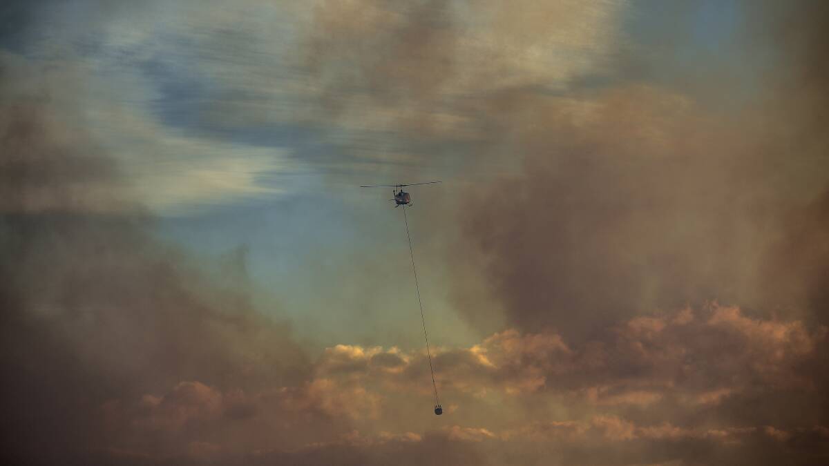 A helicopter water bombs a bushfire threatening homes in the suburbs of Voyager Point, Pleasure Point, Sandy Point, Illawong, Menai and Bangor. Picture: AAP