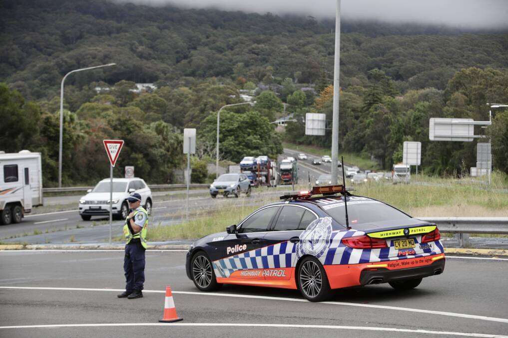 A police officer on Old Mt Ousley Road, blocking right turns onto the M1 Princes Motorway. The M1 is closed northbound due to a fallen tree branch on the road. Picture: Adam McLean