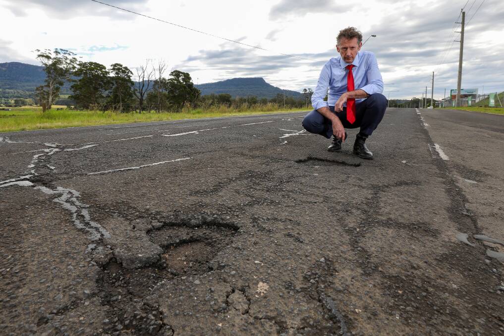 Holes: Whitlam MP Stephen Jones inspects some potholes on West Dapto Road. He said a Labor government would provide millions of dollars to repair roads nationwide. Picture: Adam McLean