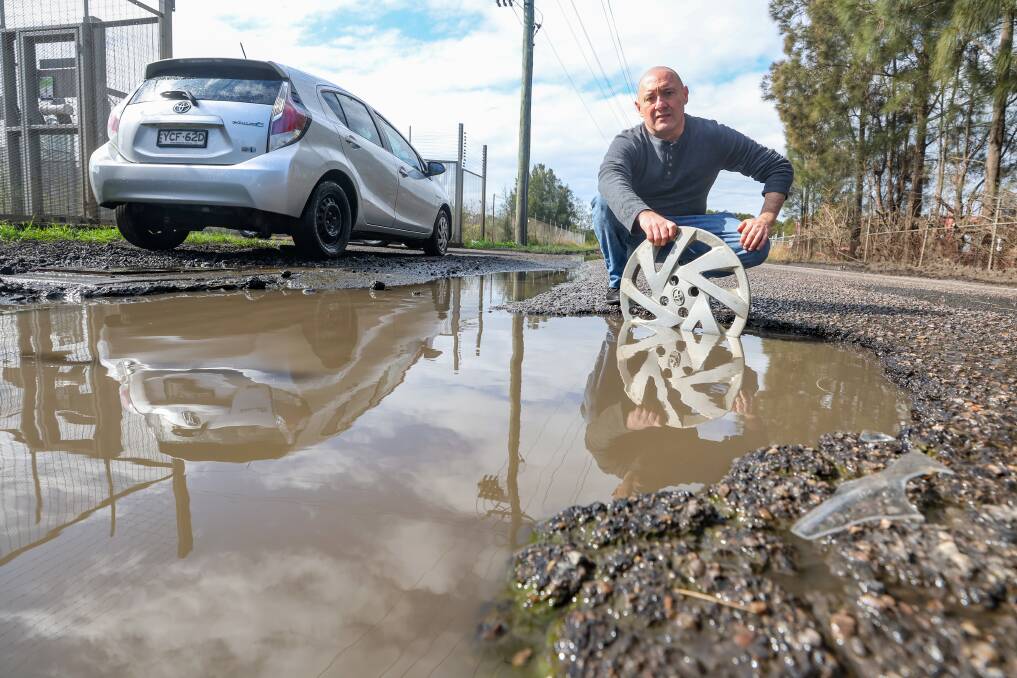 Joe Baez and the huge pothole on Reddalls Road at Kembla Grange, which caused hundreds of dollars in damage to his car. Picture by Adam McLean