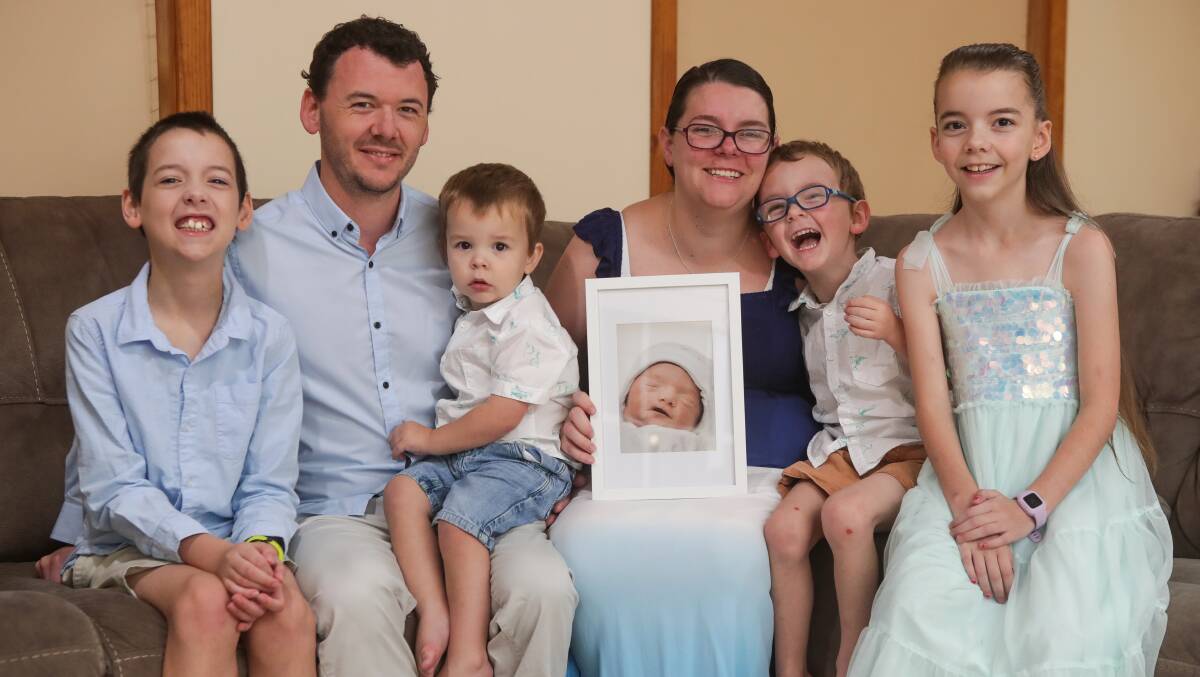 Love and loss: Rebekka and Nathan Lacey with their children Tyler, Kaleb, Blake and Charlotte. They are holding a photo of their son Flynn who died three hours after his birth in December 2021. Picture: Adam McLean