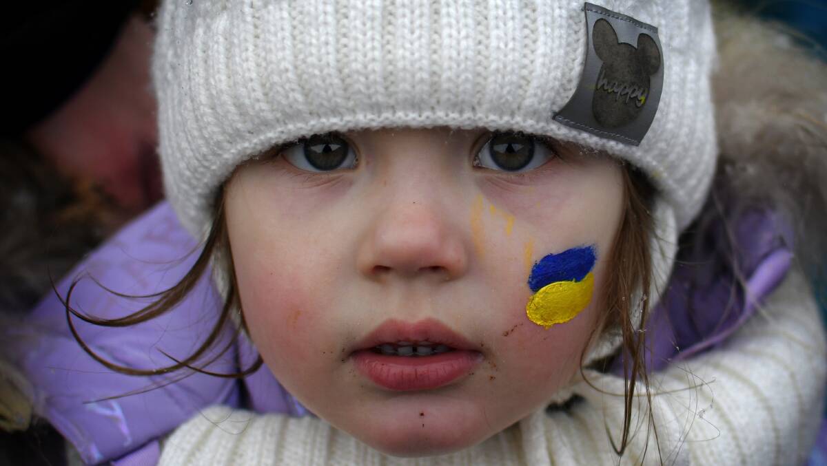 Zlata, 3, fleeing the conflict from neighboring Ukraine with her face painted in the colors of the Ukrainian flag stands at the Romanian-Ukrainian border. Photo: AP Photo/Andreea Alexandru