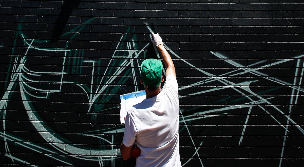 Words on the street: Adelaide artist Vans the Omega outlines part of his mural on the back wall of Piccadilly Motor Inn. Pictures: Adam McLean.