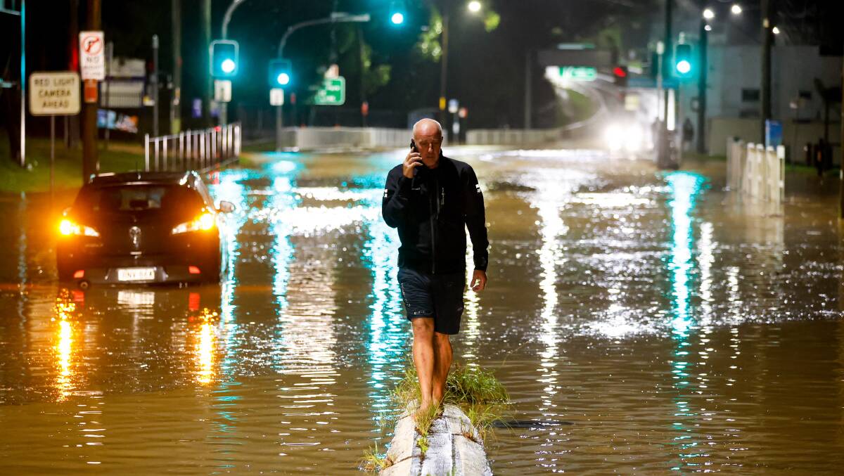 Floodwaters cover the Princes Highway in Bulli at around 6am Saturday morning. A man calls his daughter to let her know he can't pick her up as he is cut off. Picture by Anna Warr