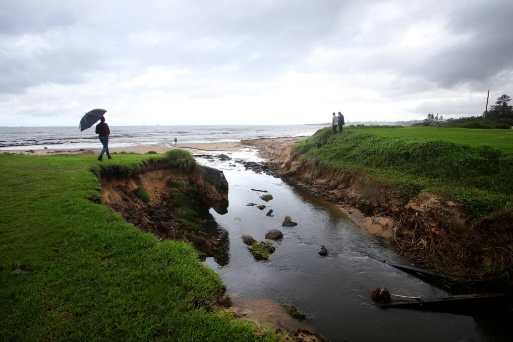 FLOOD DAMAGE: Onlookers survey a scarped creek near Henley Road in Thirroul on Sunday, with large chunks of debris left behind after the storm such as timber and concrete. Picture: Sylvia Liber